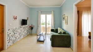 A living room with a green sofa, a coffee table, a flat-screen TV, and a view of the outdoors through a glass door. - Poseidon Apartments (Chania)