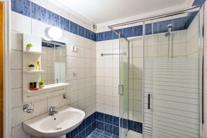 Un baño con ducha de vidrio, lavamanos blanco y un espejo sobre él.