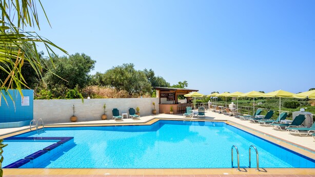 A rectangular swimming pool with clear blue water, surrounded by lounge chairs and umbrellas, and a small bar area with outdoor seating. - Poseidon Apartments (Chania)