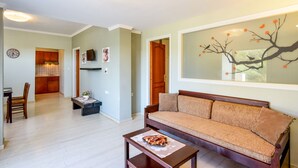 A living room with a sofa, a coffee table, and a dining area with a chair and table. - Poseidon Apartments (Chania)