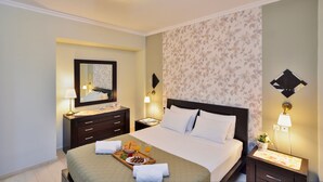 A hotel room with a bed, a nightstand, a dresser, a mirror, and a floral wallpaper. - Poseidon Apartments (Chania)