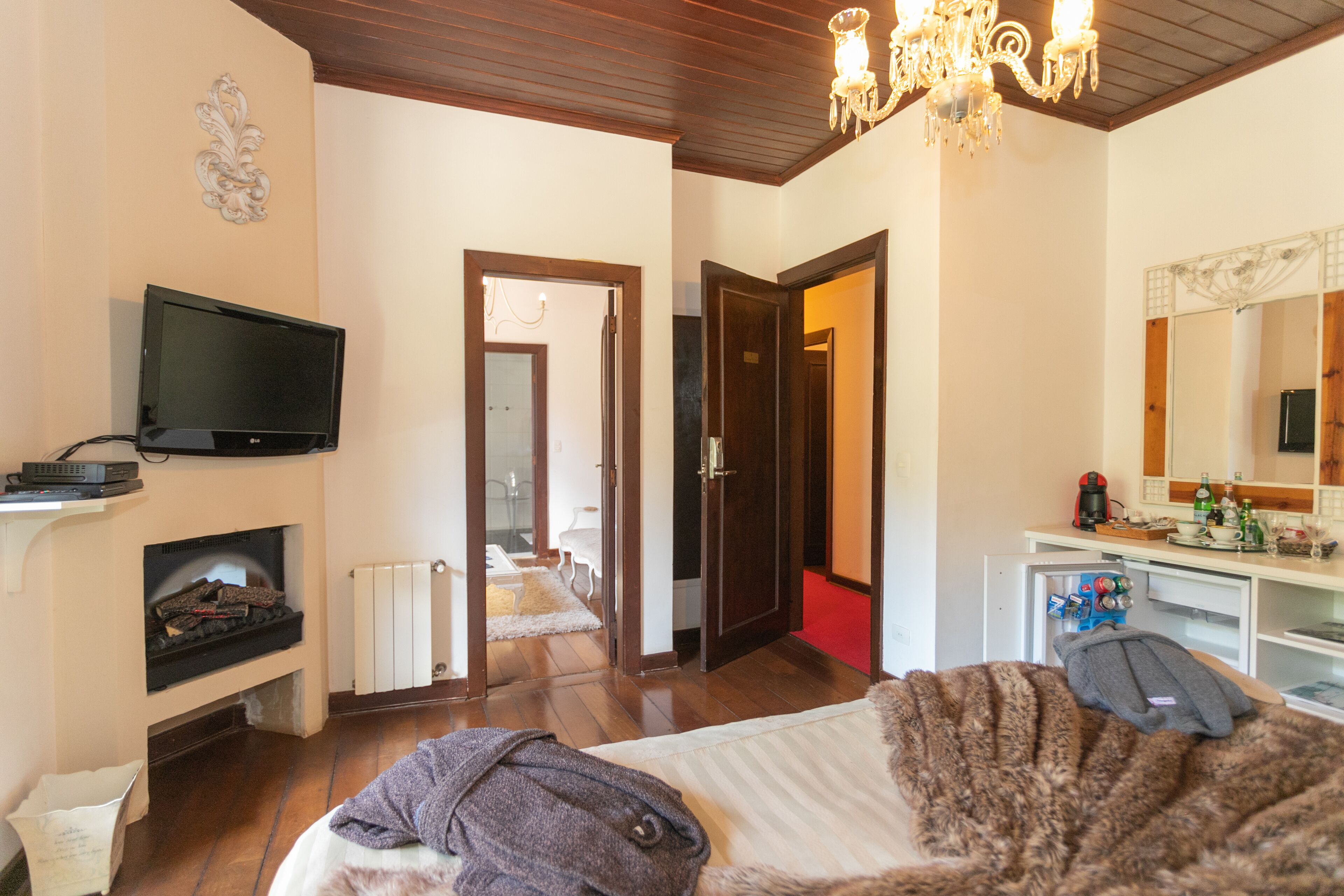 A hotel room with a television, fireplace, bed, and a mirror.