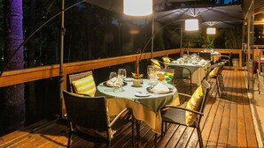 An outdoor dining area with tables and chairs under large umbrellas, surrounded by wooden deck and trees. - Villa Casato Residenza Boutique (Campos do Jordão)