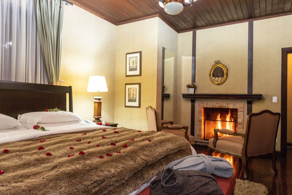 Habitación de hotel con cama, chimenea, sillón y espejo en la pared.