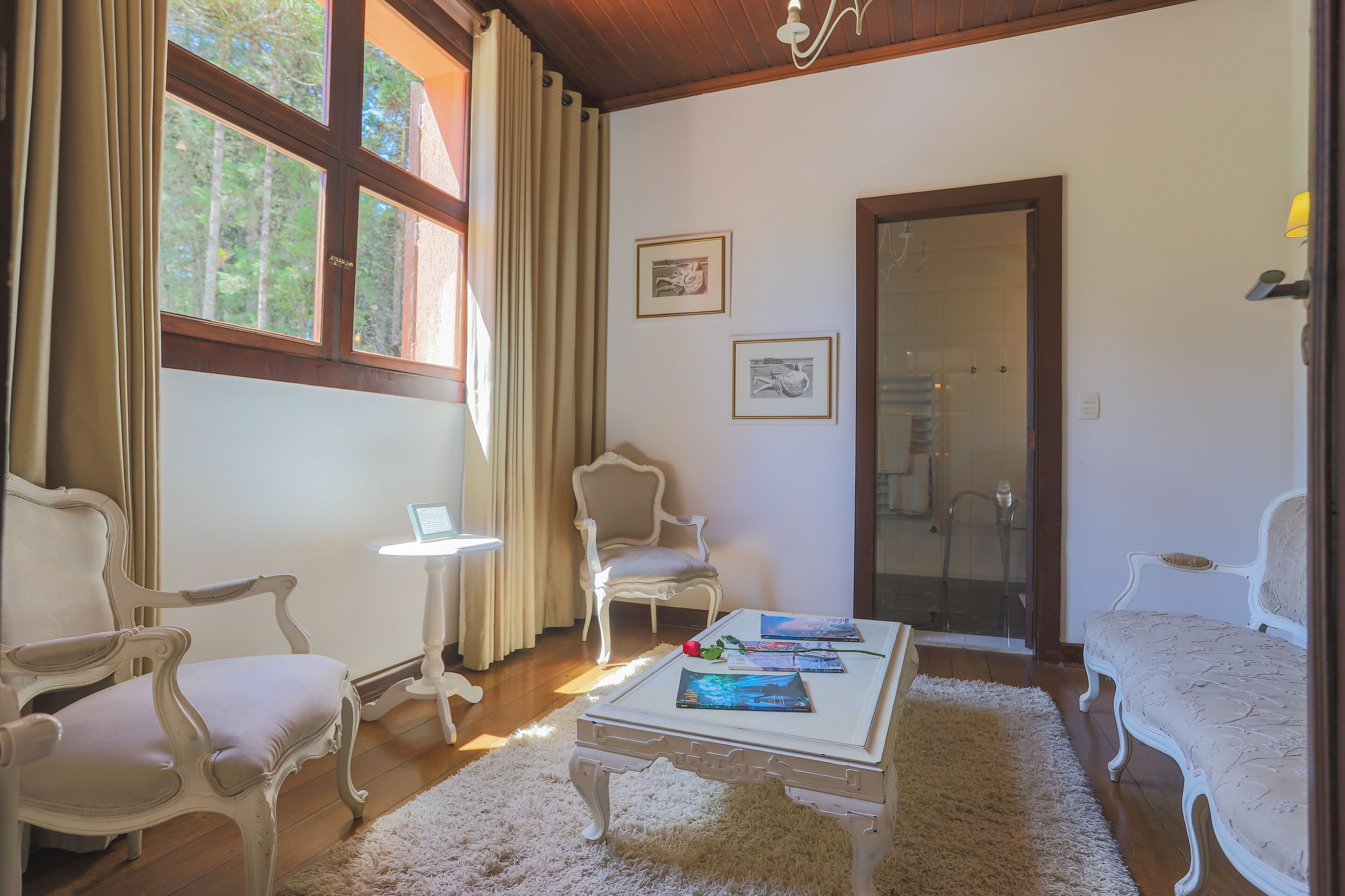A room with two white upholstered chairs, a white table with magazines, a small white side table, and a glass door leading to a shower area.