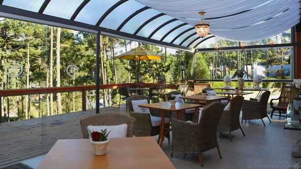 An outdoor dining area with wicker furniture and a glass ceiling, overlooking a forested area. - Villa Casato Residenza Boutique (Campos do Jordão)