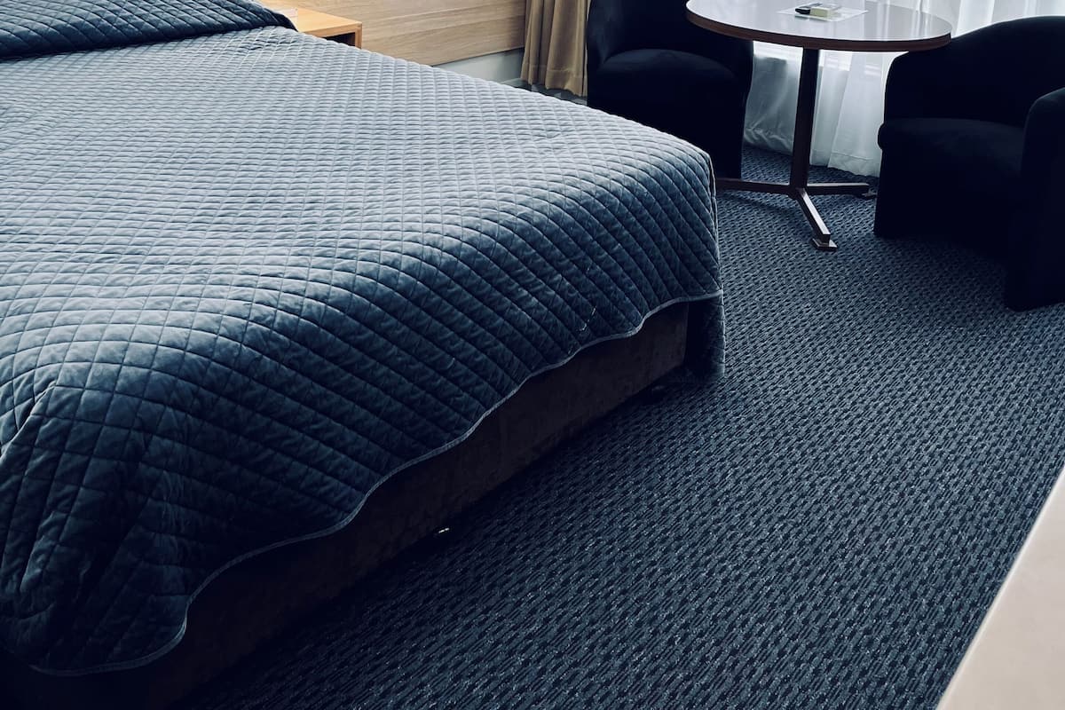 Une chambre d’hôtel avec un lit, deux chaises, une petite table, une lampe et un tableau représentant une scène de plage.