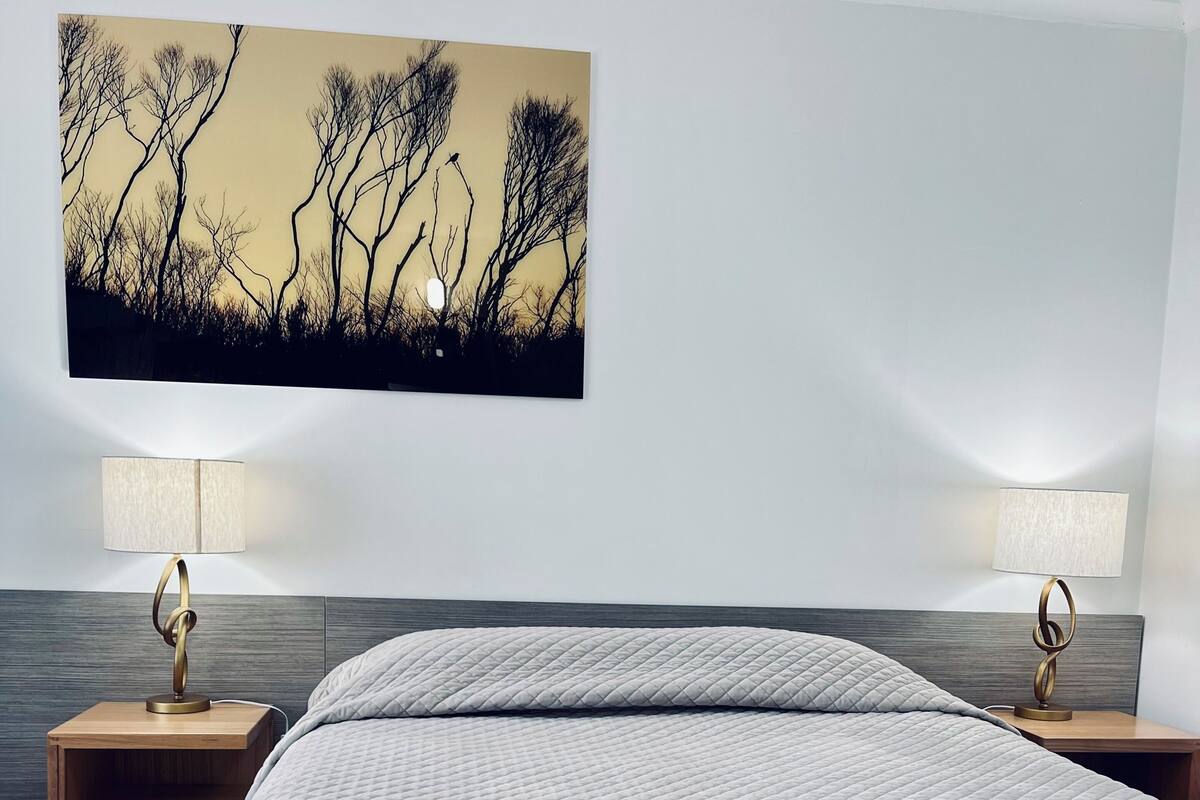 Une chambre d’hôtel avec un grand lit, deux tables de chevet avec des lampes, un tableau accroché au mur et une tête de lit en bois.