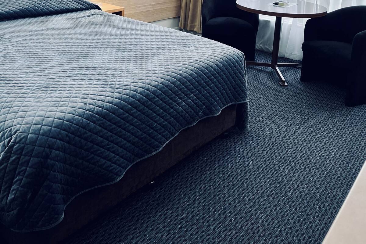 Une chambre d’hôtel avec un lit, deux chaises, une petite table, une lampe et un tableau représentant une scène de plage.