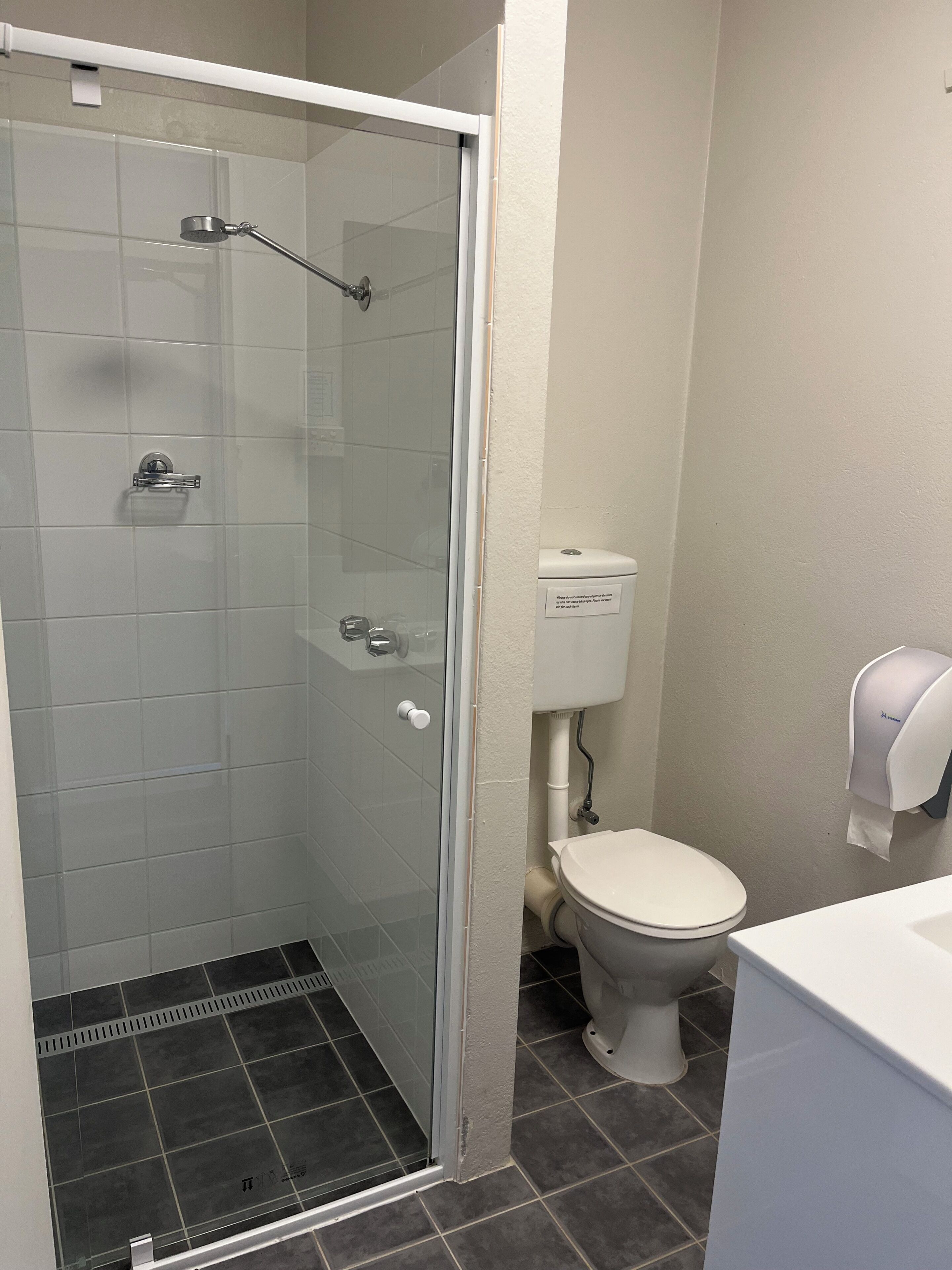 A bathroom with a glass-enclosed shower, a toilet, and a paper towel dispenser.