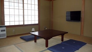 A traditional Japanese room with tatami mats, a low table, a heater, and a TV mounted on the wall. - K's House Hakuba Alps - Hostel (Hakuba)