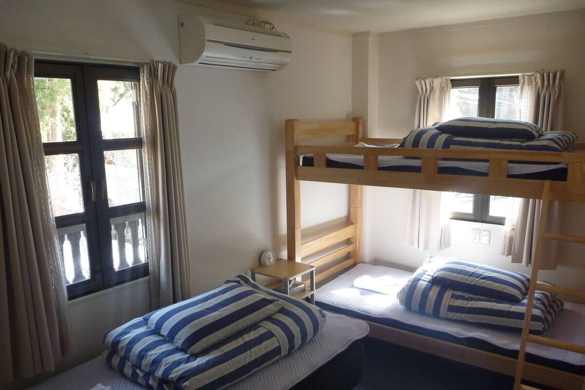 A bunk bed room with a window, an air conditioning unit, and a small table with a clock.