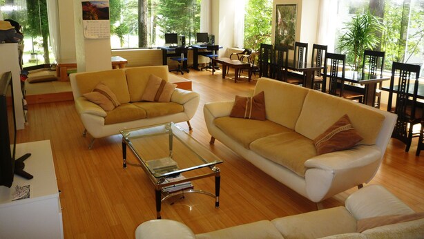 A spacious living area with two sofas, a coffee table, and a dining table with chairs. There is a large window providing a view of greenery outside. - K's House Hakuba Alps - Hostel (Hakuba)