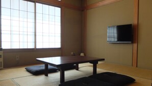 A traditional Japanese room with tatami flooring, a low table, cushions, and a mounted television. - K's House Hakuba Alps - Hostel (Hakuba)
