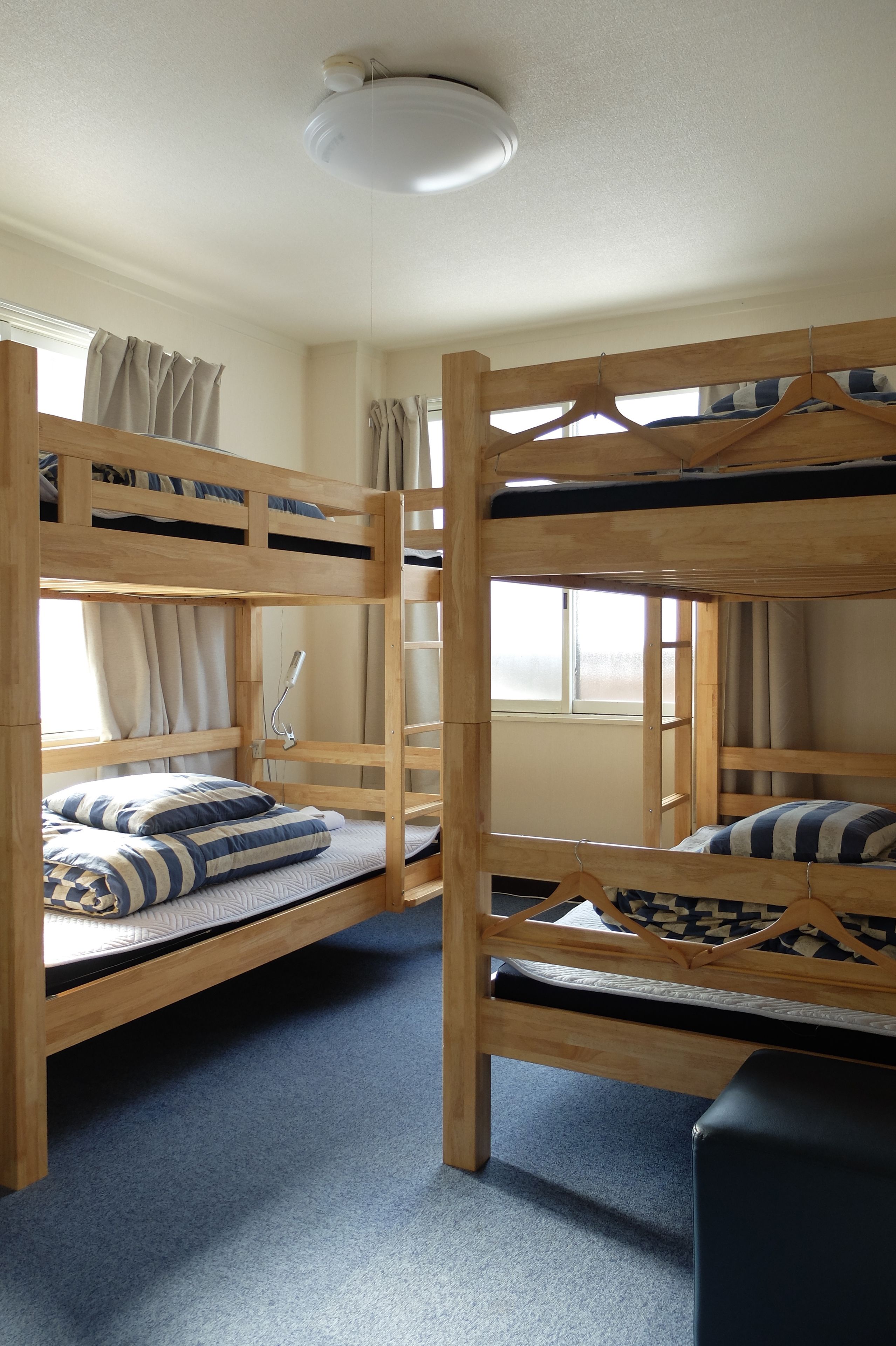 Une chambre avec un lit superposé, un ventilateur de plafond, des lits superposés en bois et une fenêtre avec des rideaux.