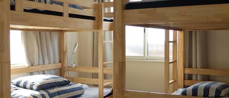 Une chambre avec un lit superposé, un ventilateur de plafond, des lits superposés en bois et une fenêtre avec des rideaux.