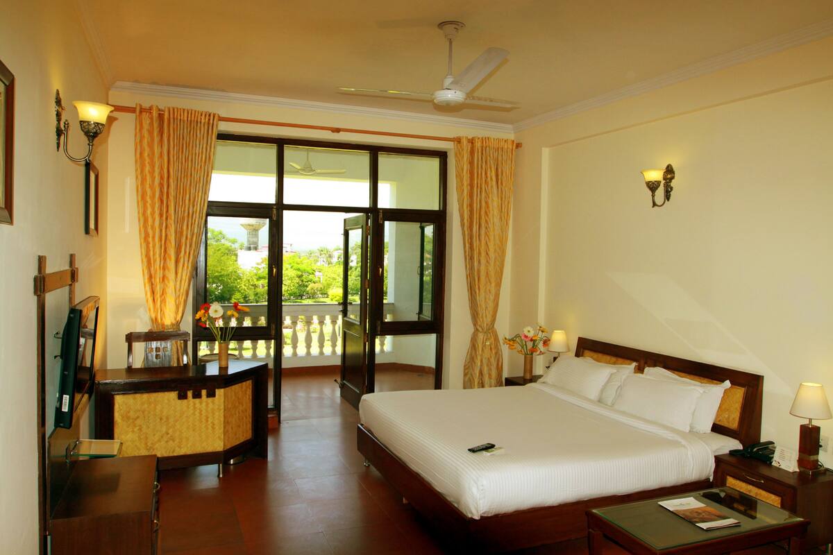 A hotel room with a large bed, a desk, a chair, a nightstand, a lamp, and a ceiling fan.