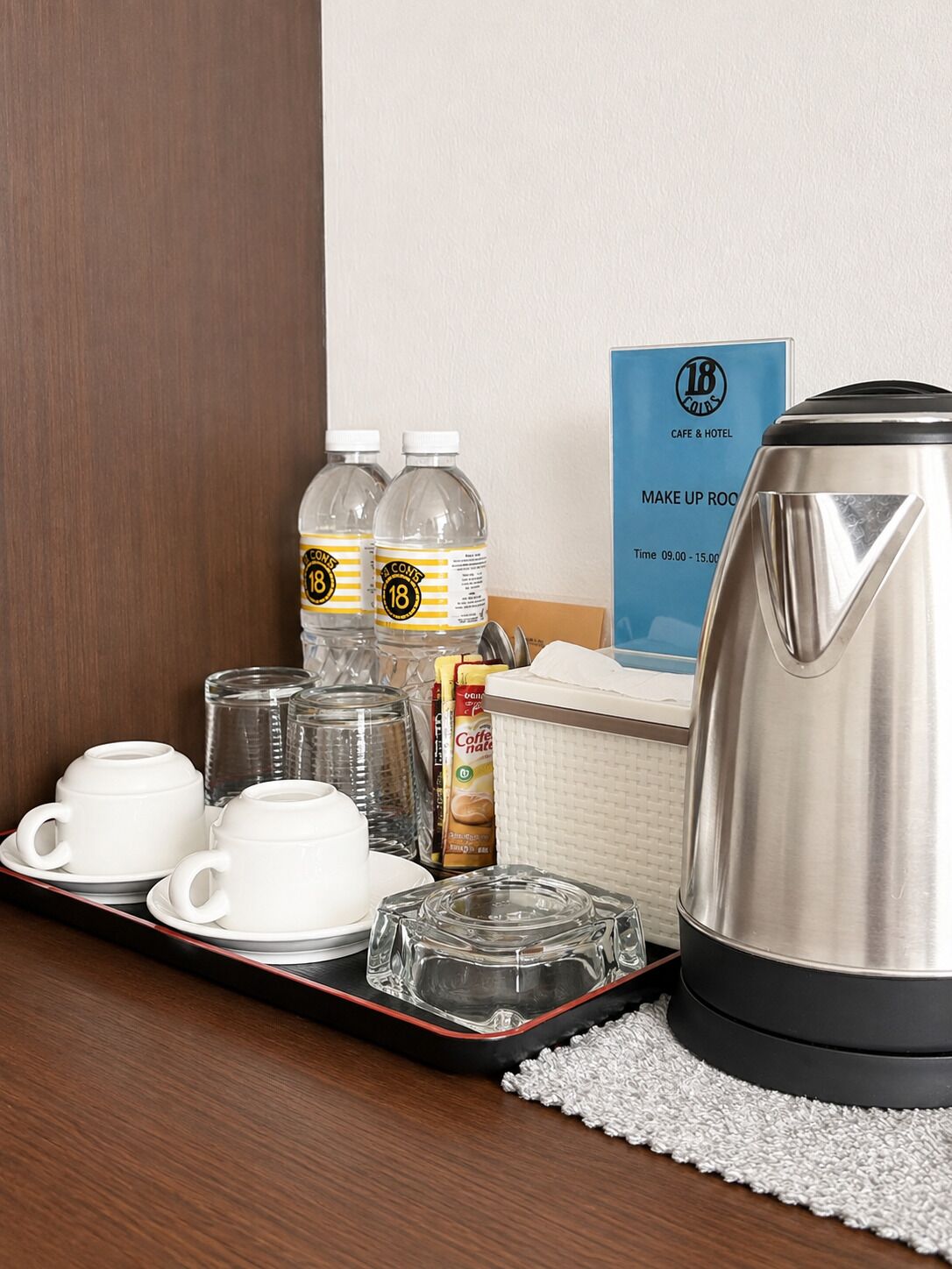 A hotel room's breakfast setup with a tray containing coffee cups, a kettle, water bottles, and a coffee maker.