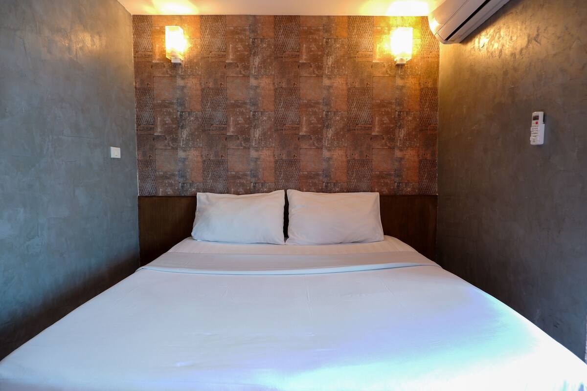 A single bed with white linens in a room with textured walls and two wall-mounted lights.