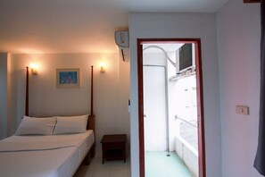 A bedroom with a bed, bedside lamps, a small table, a picture on the wall, and an air conditioning unit. - 18 Coins Budget Hotel (Pattaya)