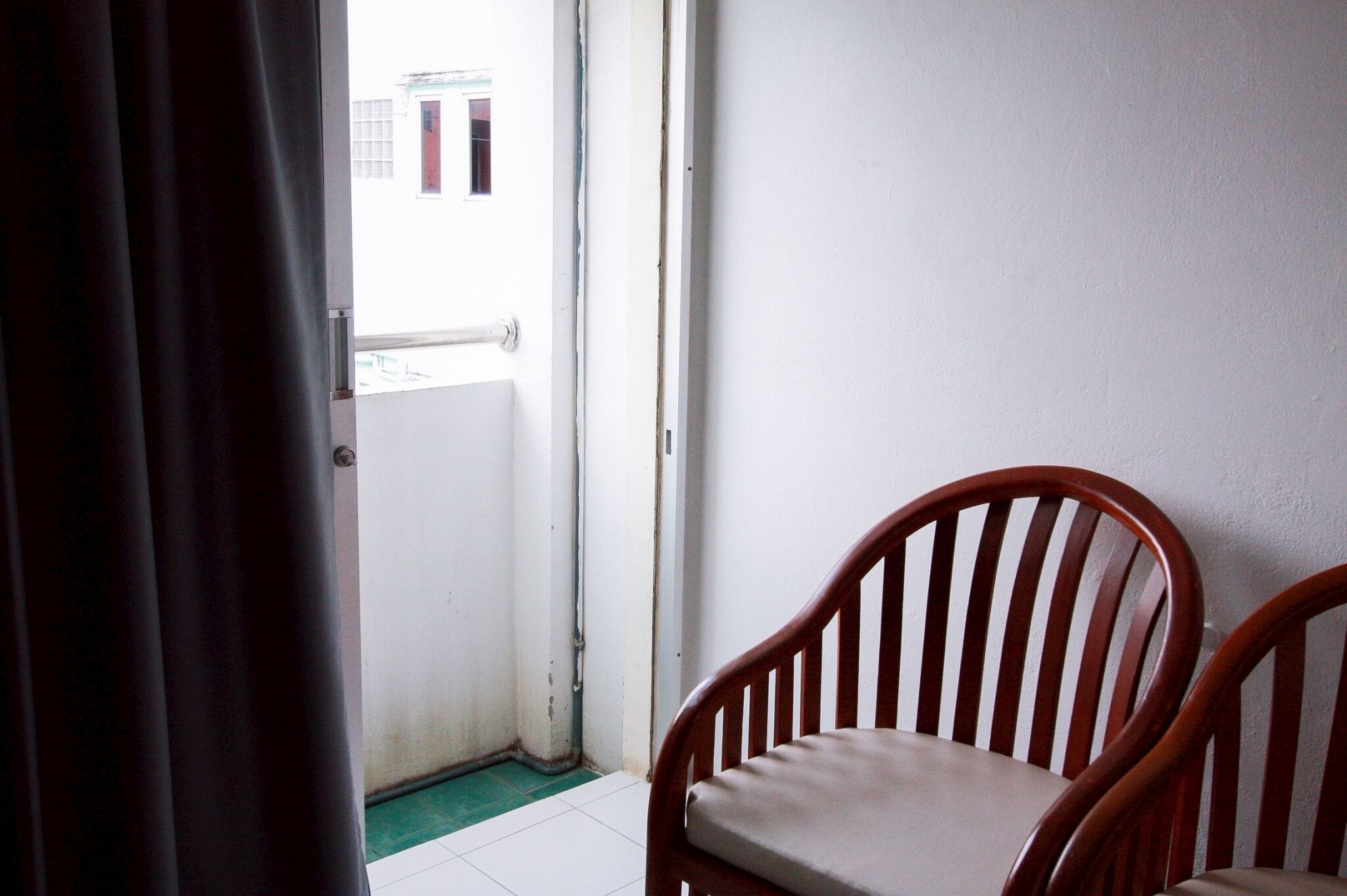 A room with a wooden chair, a white door, and a view of a building outside.