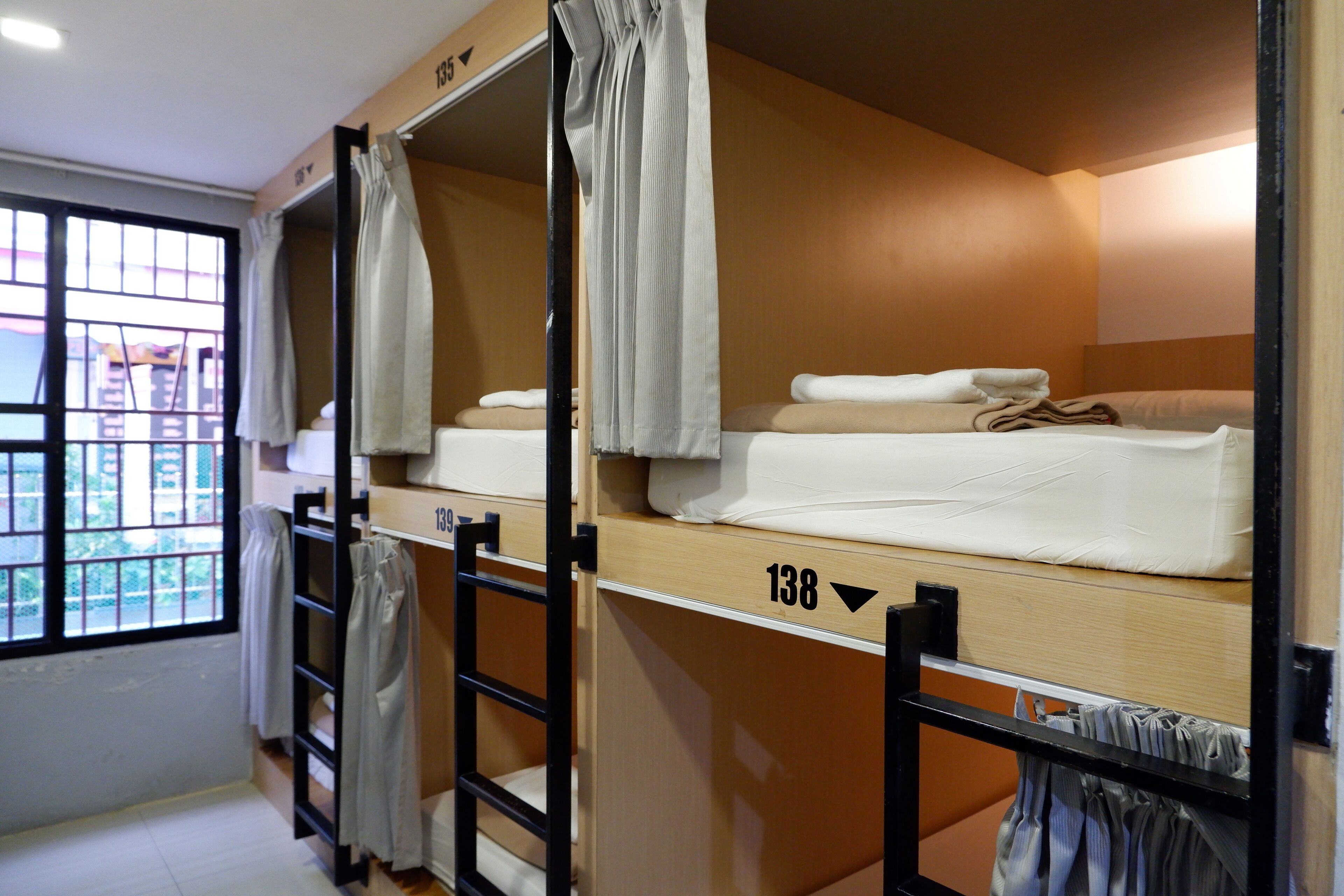 A dormitory room with bunk beds, a window with curtains, and a visible room number.