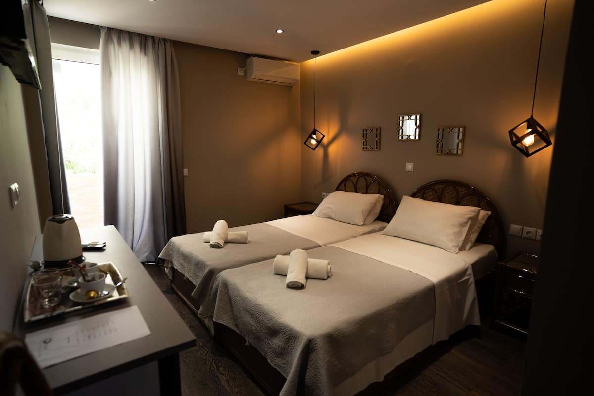 A hotel room with two beds, a desk with a tray of breakfast items, and a window with curtains.