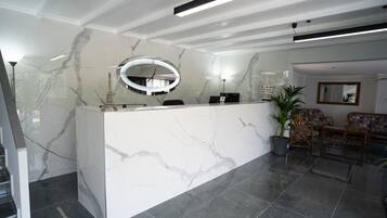 Un área de recepción con un mostrador de mármol, un espejo redondo y un espacio de espera con muebles de mimbre.