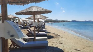 A beach with sun loungers and umbrellas, a clear sky, and a calm sea.