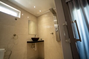 A modern bathroom with a large mirror, a vessel sink, and a shower area.