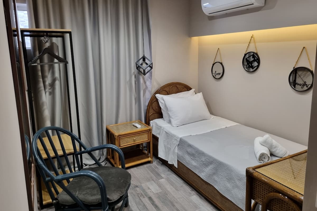 A hotel room with a bed, a chair, a nightstand, and a wall-mounted air conditioner.