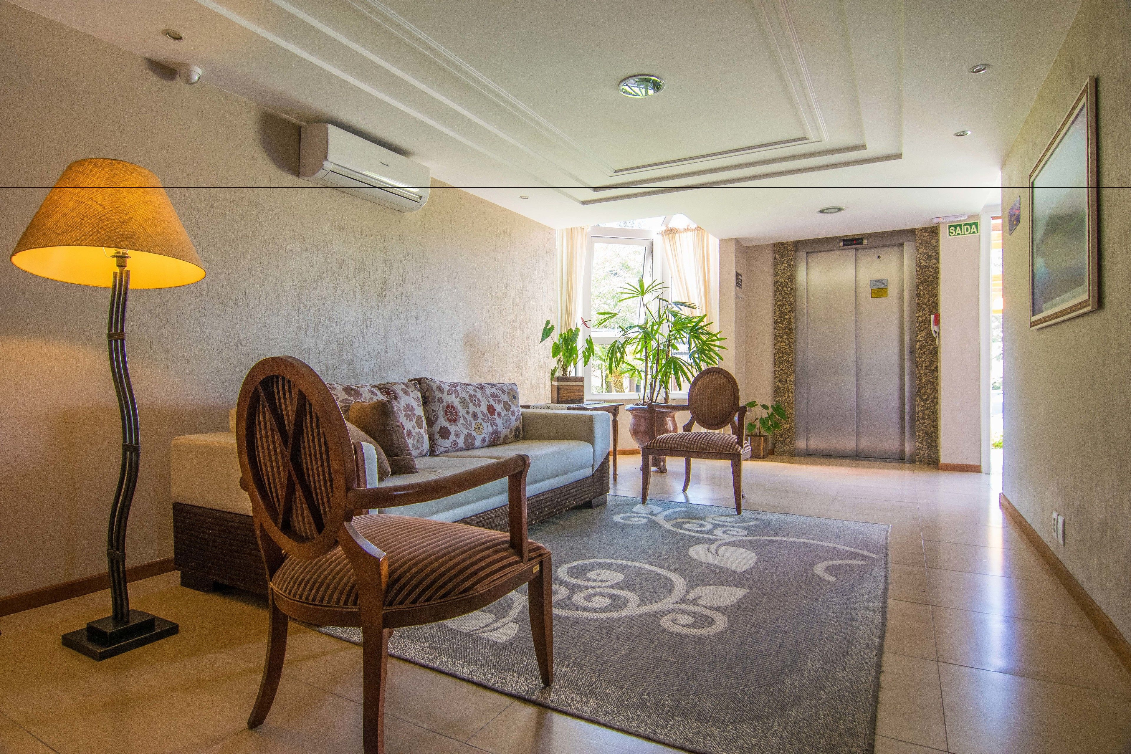 Een hotellobby met een bank, stoelen, een lamp, een potplant en een lift.