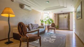 Een hotellobby met een bank, stoelen, een lamp, een potplant en een lift.