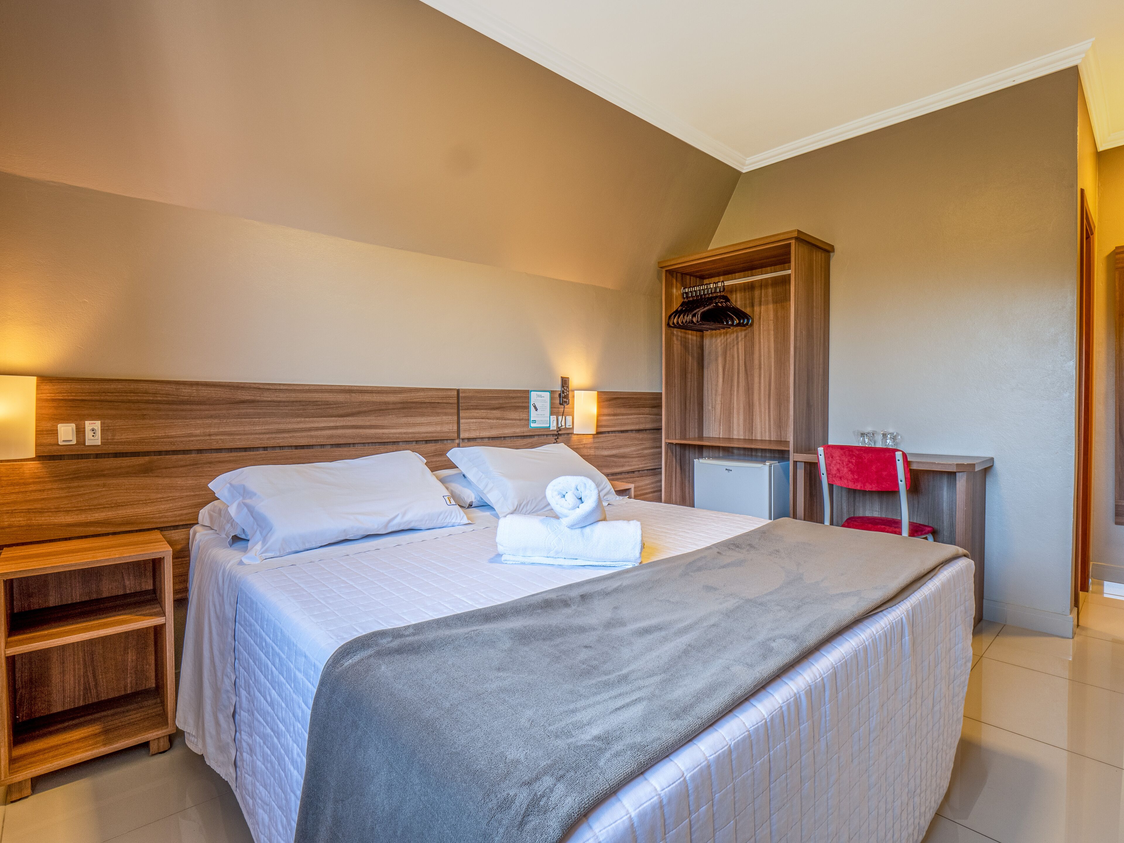 A hotel room with a bed, bedside tables, a wardrobe, and a desk with a chair.