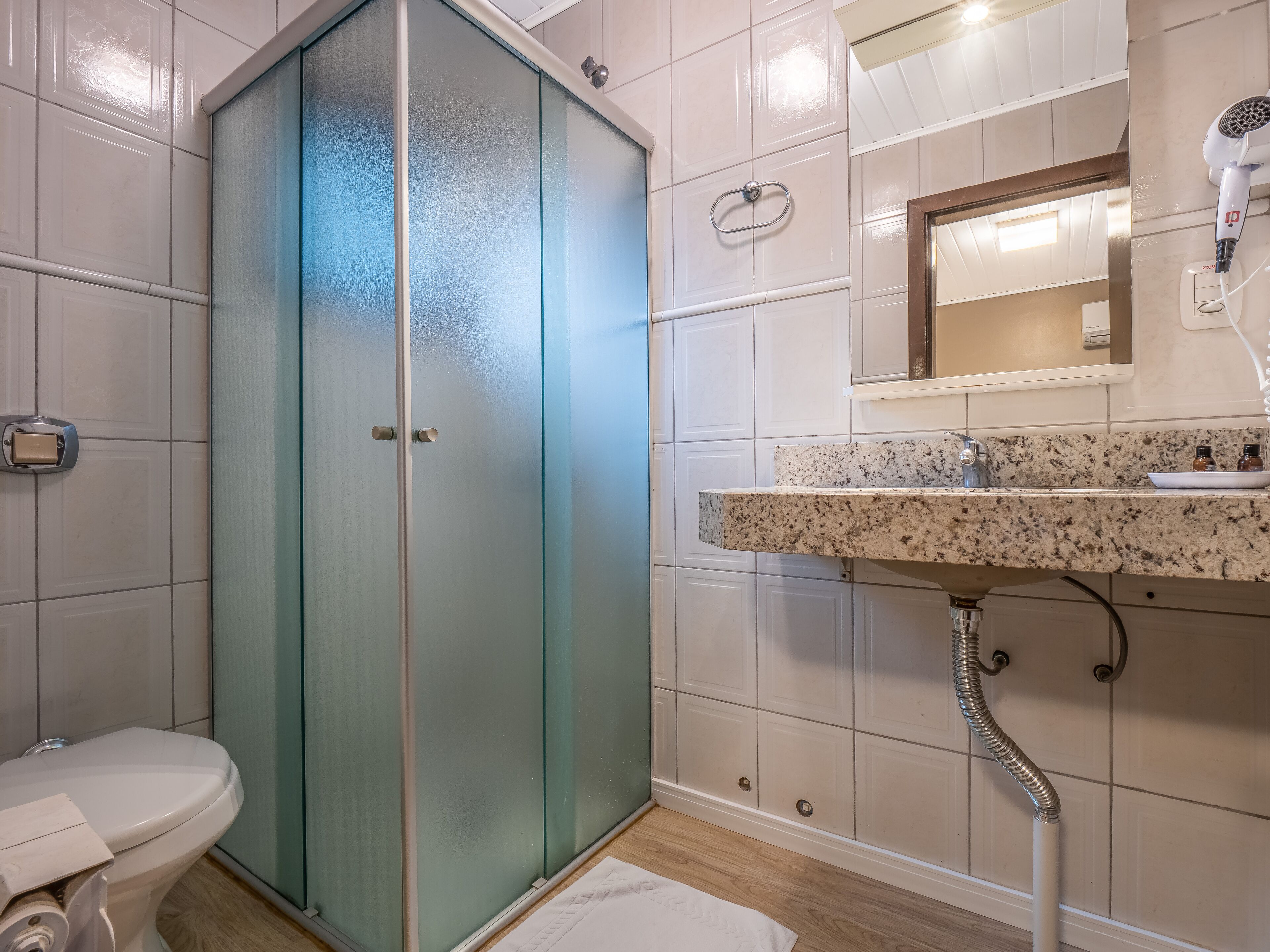 Un baño con cabina de ducha de vidrio, un inodoro, un lavabo con encimera de mármol y un espejo sobre el lavabo.