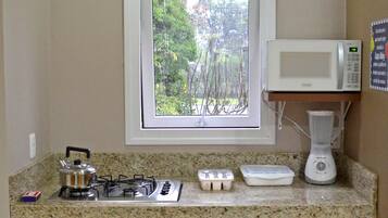 A kitchen with a gas stove, microwave, and a window with a view of greenery.