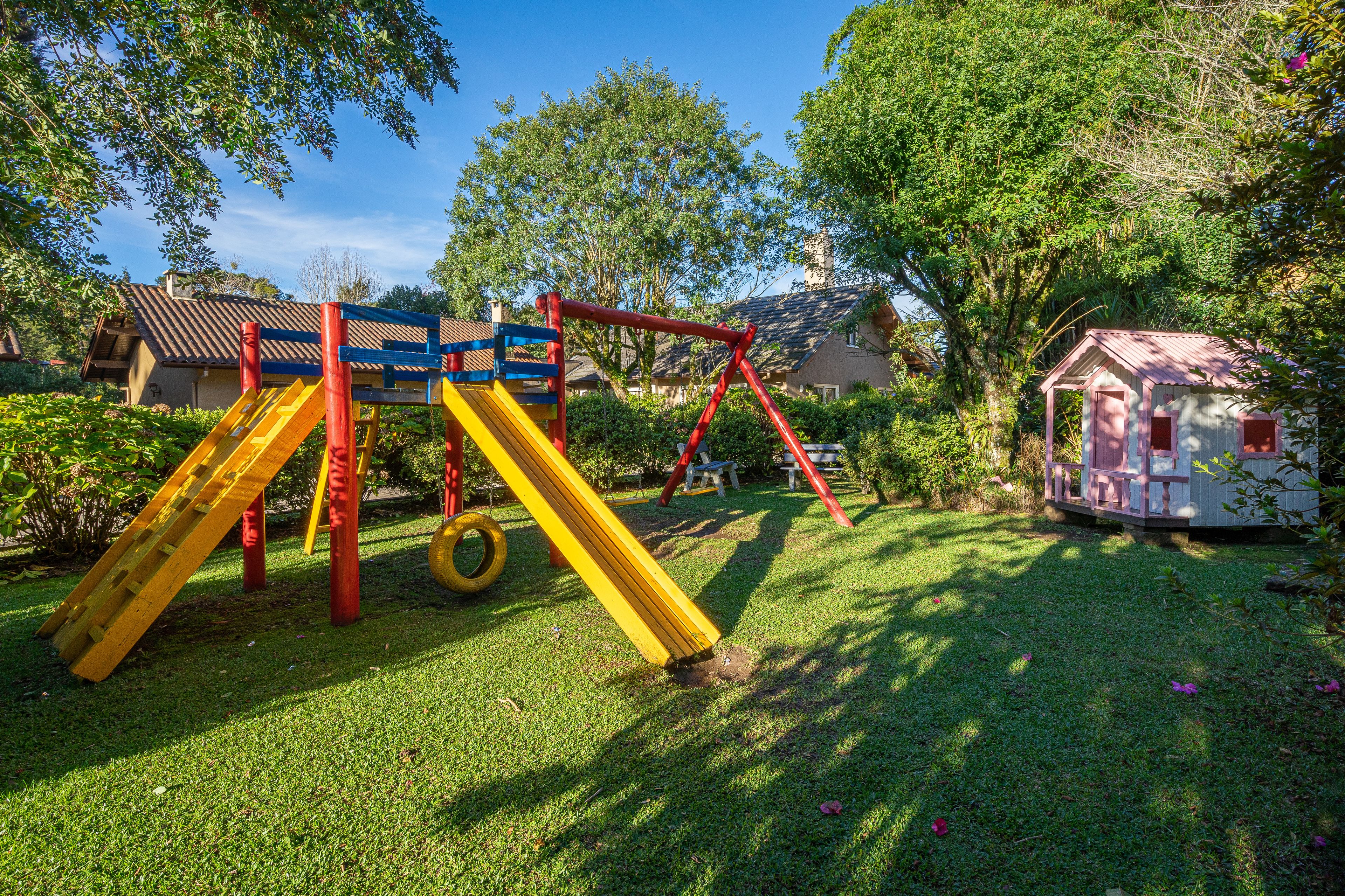 Un parque infantil con tobogán, columpios y una pequeña estructura que parece una casa.