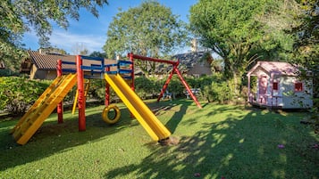 Un parque infantil con tobogán, columpios y una pequeña estructura que parece una casa.