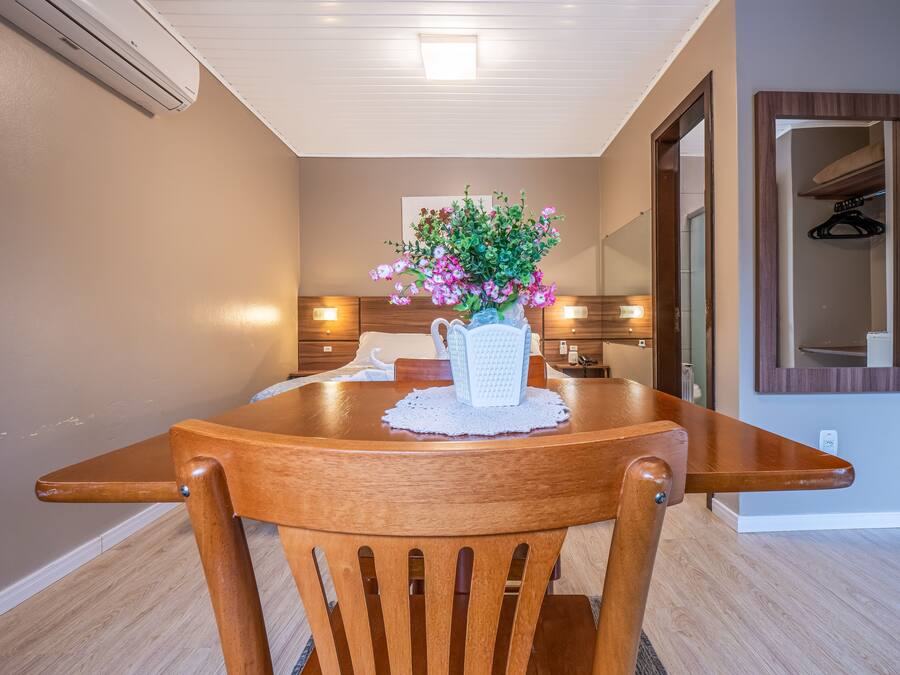 Un comedor con una mesa de madera, sillas, un jarrón de flores y un espejo en la pared.