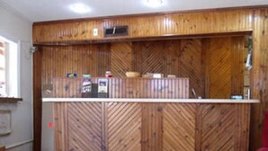 A reception area with a wooden panel wall, a reception desk, and a patterned carpet. - Woodlawn Hills Motel (Henderson)