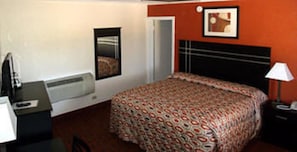 A hotel room with a bed, a desk, a chair, a window, and a door.