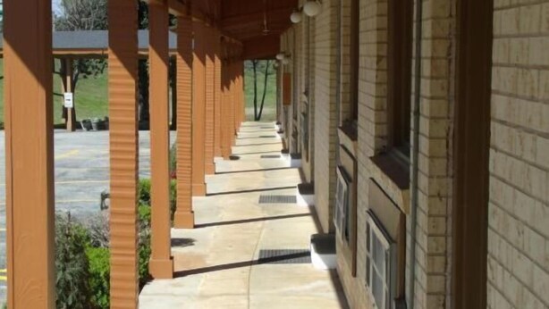 A covered outdoor corridor with a brick wall on one side and a wooden structure on the other. - Woodlawn Hills Motel (Henderson)