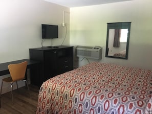 A bedroom with a bed, a desk, a chair, a television, an air conditioner, and a window with curtains.