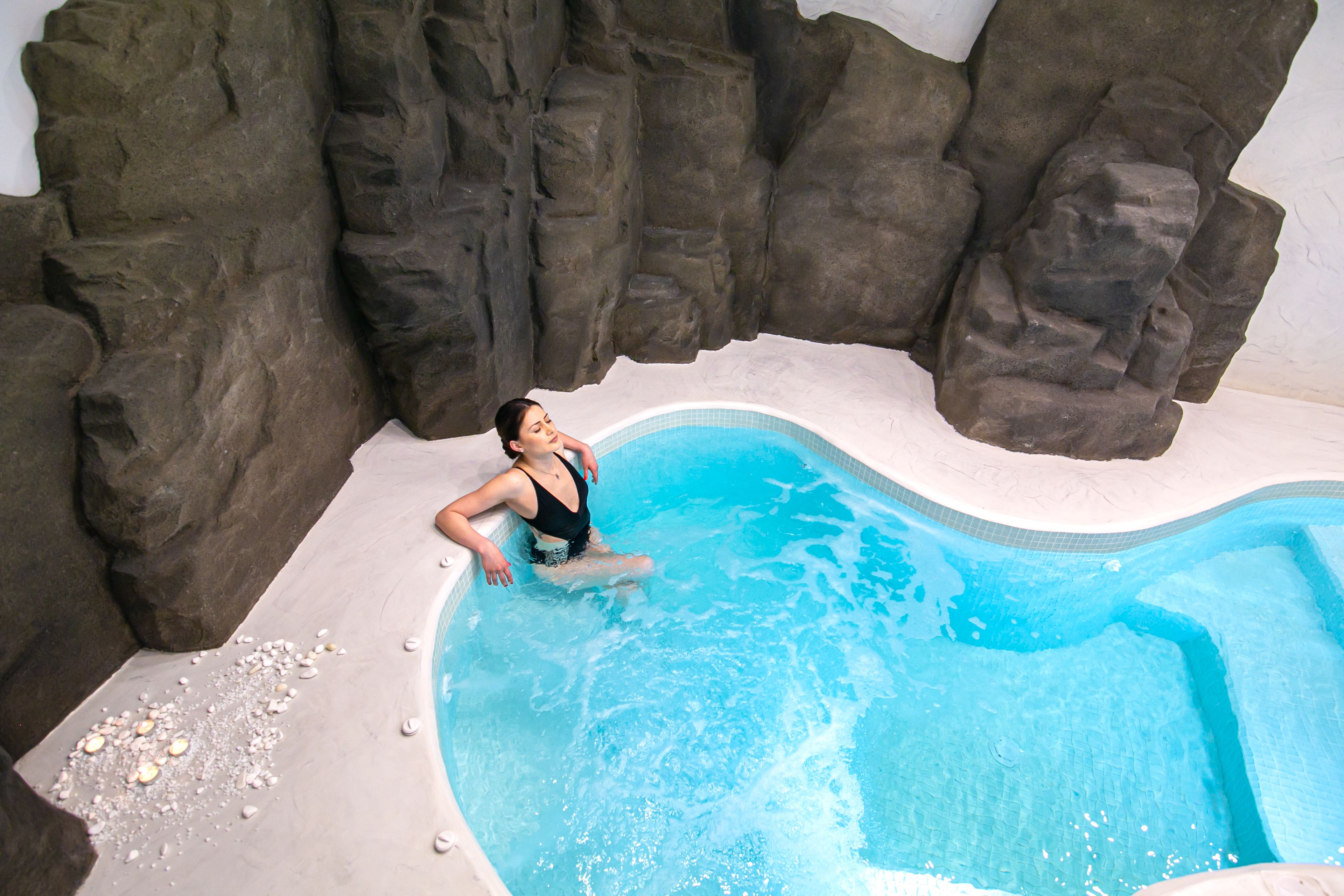 Une personne dans une piscine, avec un mur rocheux en arrière-plan.