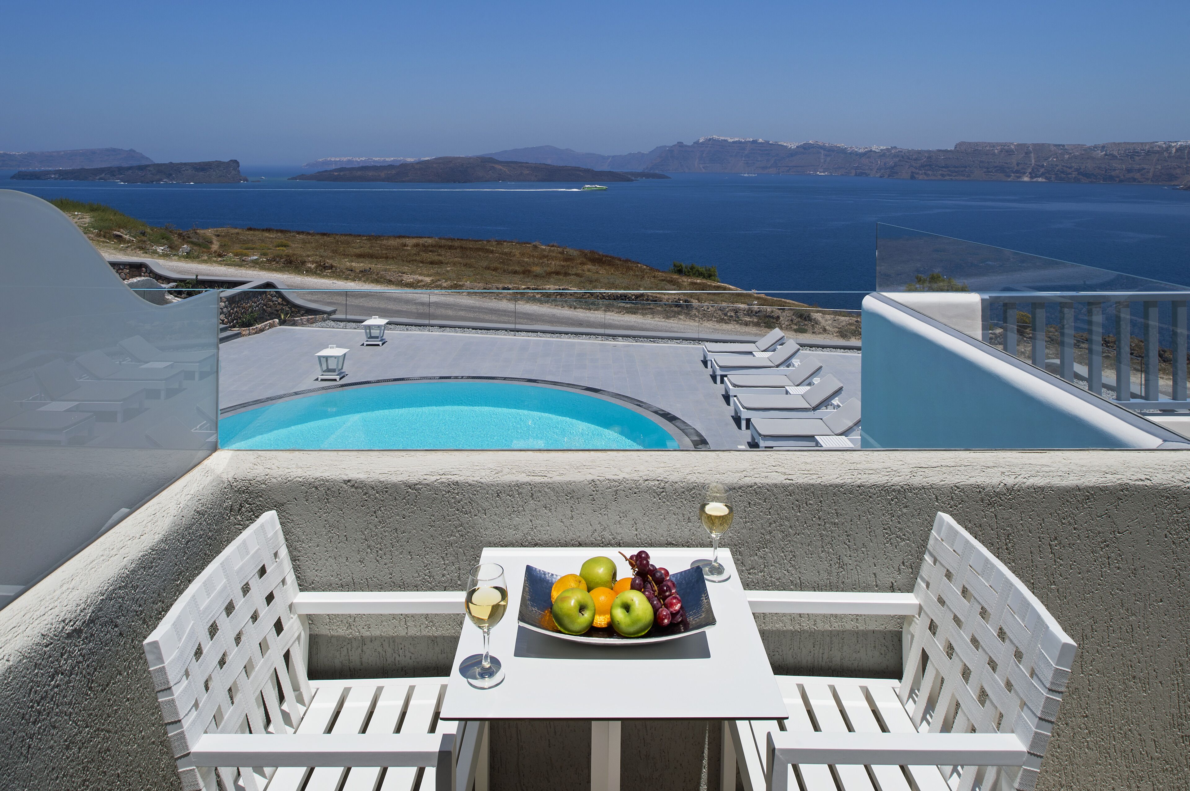Un balcon avec une table dressée pour deux personnes, une piscine et une vue sur la mer et les falaises.