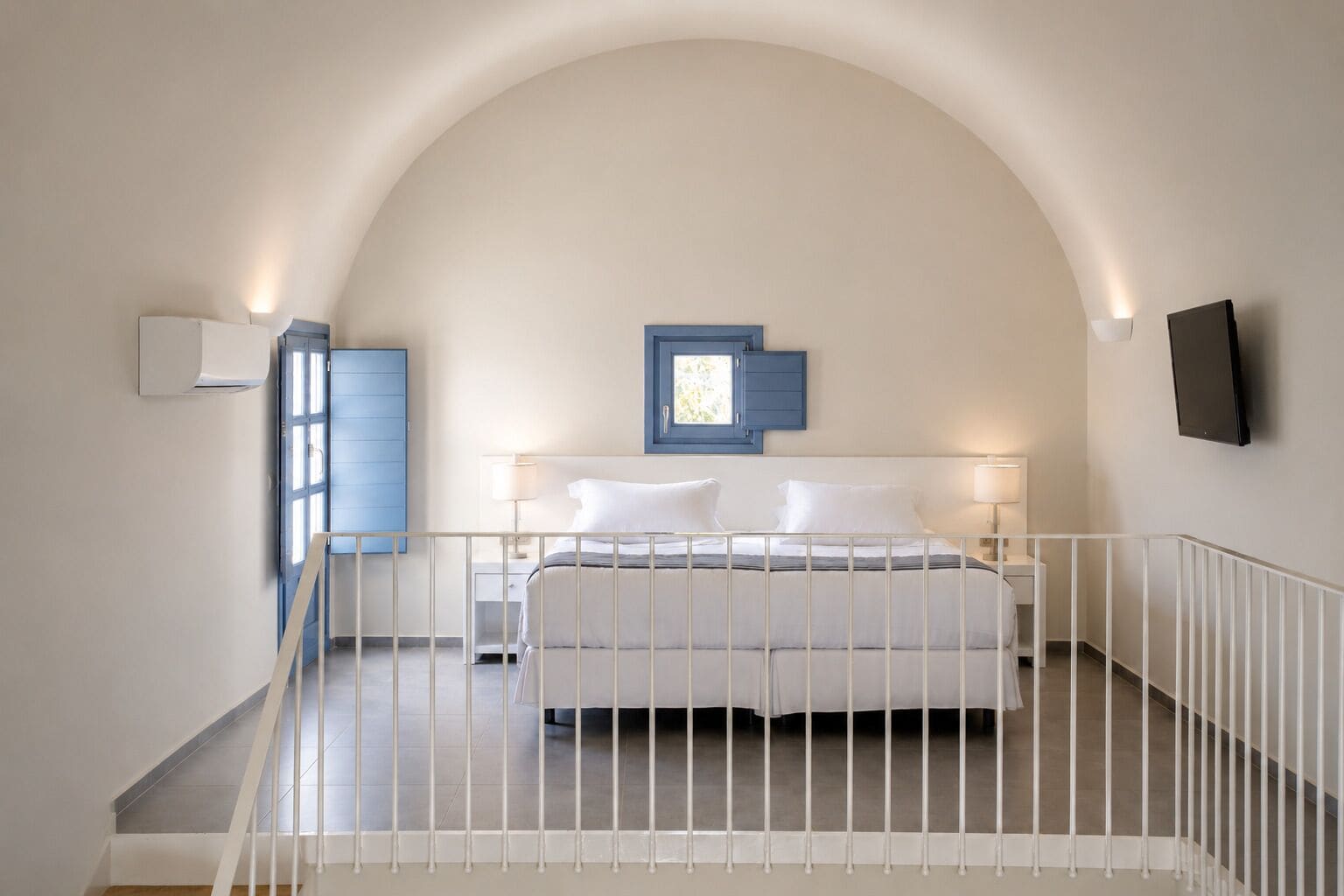 Een slaapkamer met een bed, een raam, een televisie en een trap.