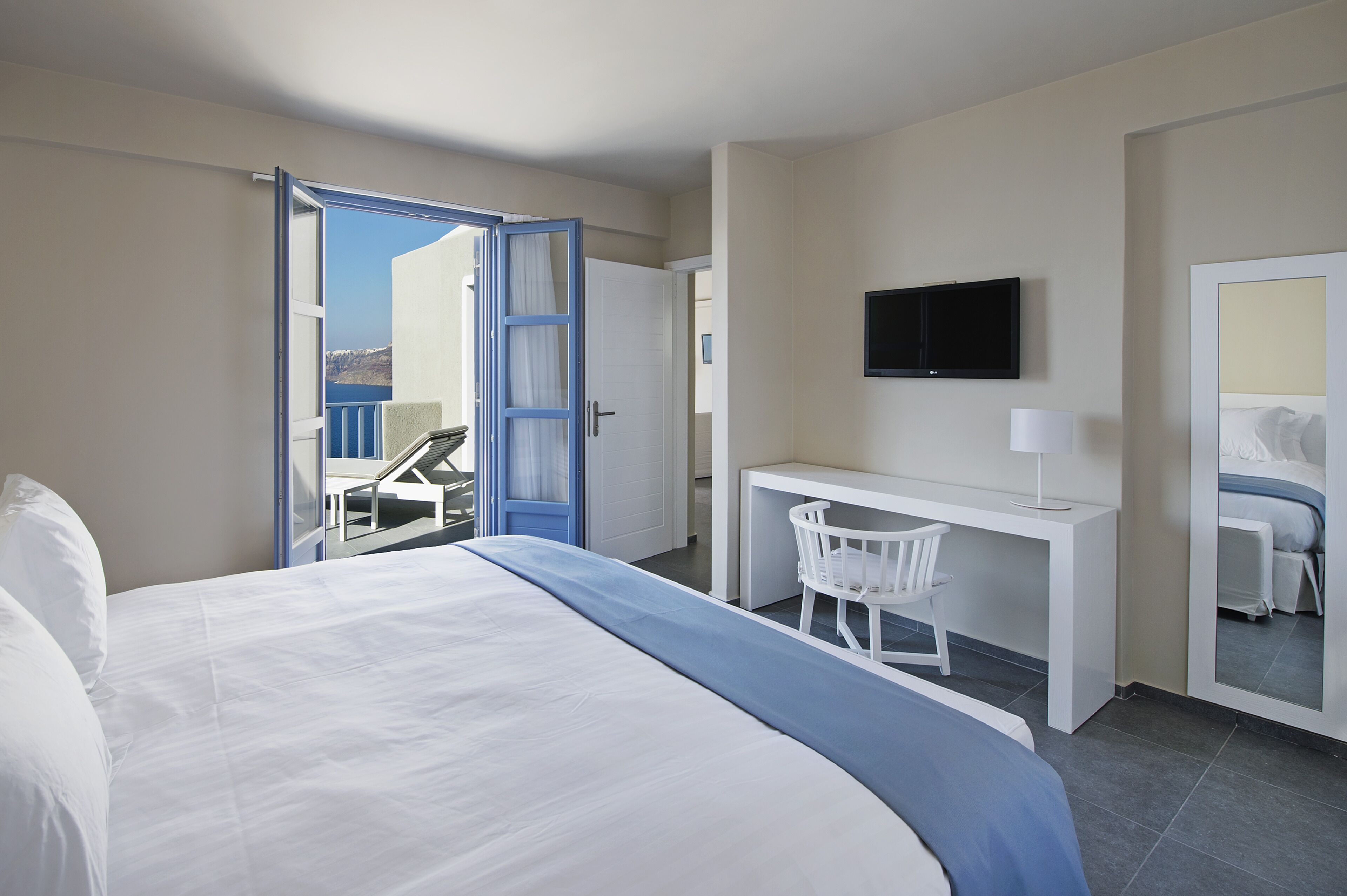 Une chambre d’hôtel équipée d’un lit, d’un bureau, d’une chaise, d’une télévision et d’un balcon avec vue.