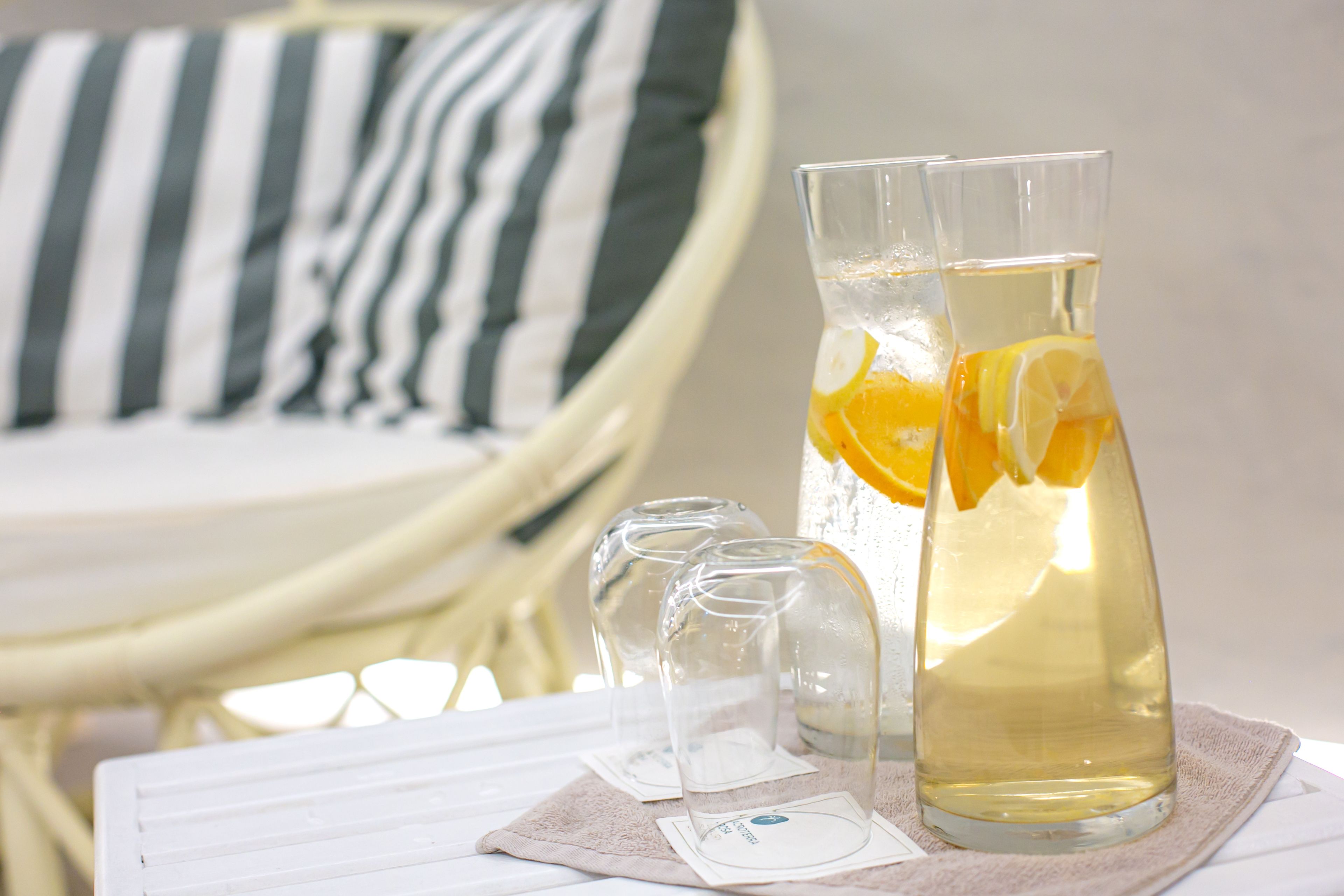 Two clear glasses on a table with a white cloth, one with a lemon slice.