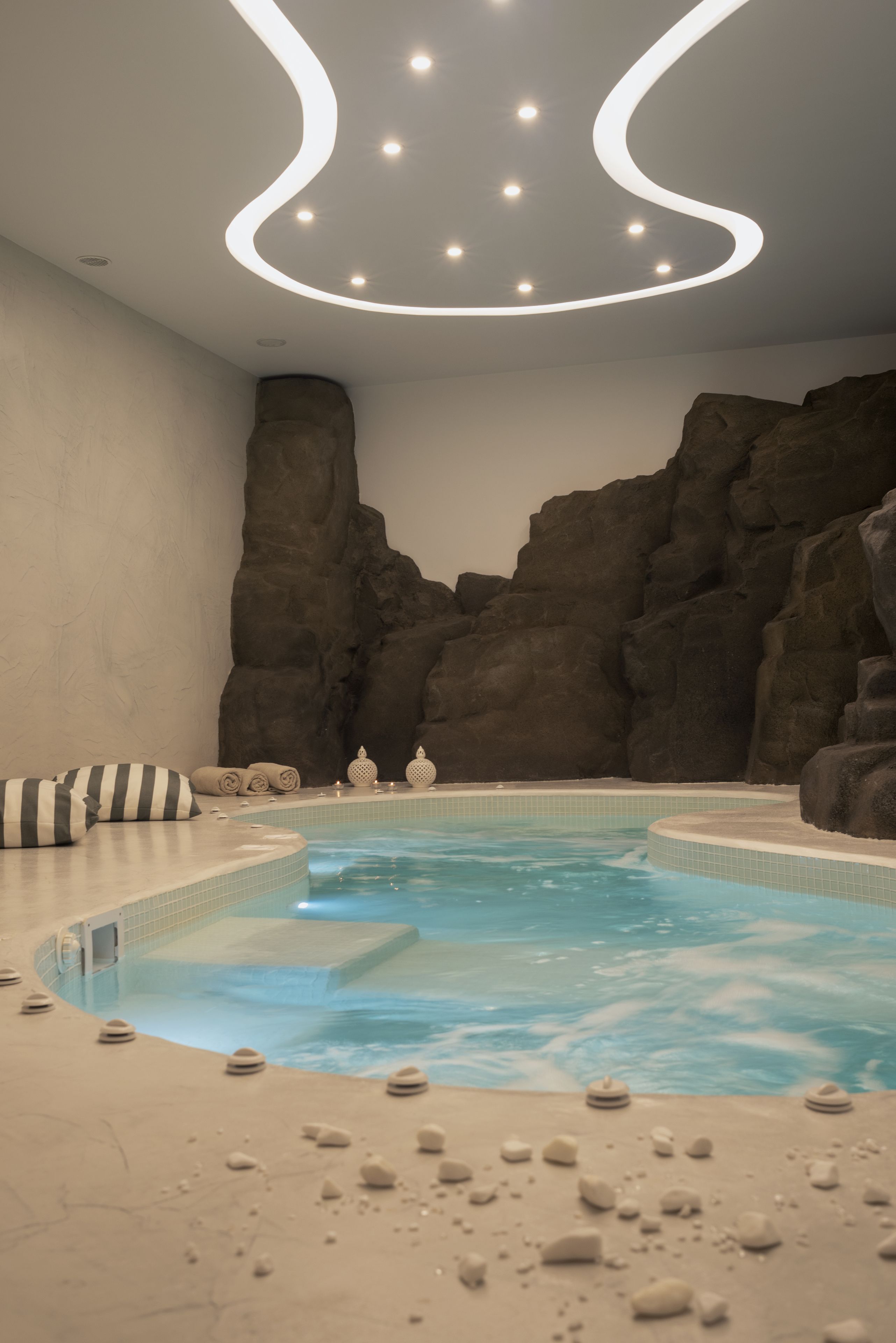 Ein Wellnessbereich mit Whirlpool, beigen Fliesen und einer Steinwand.