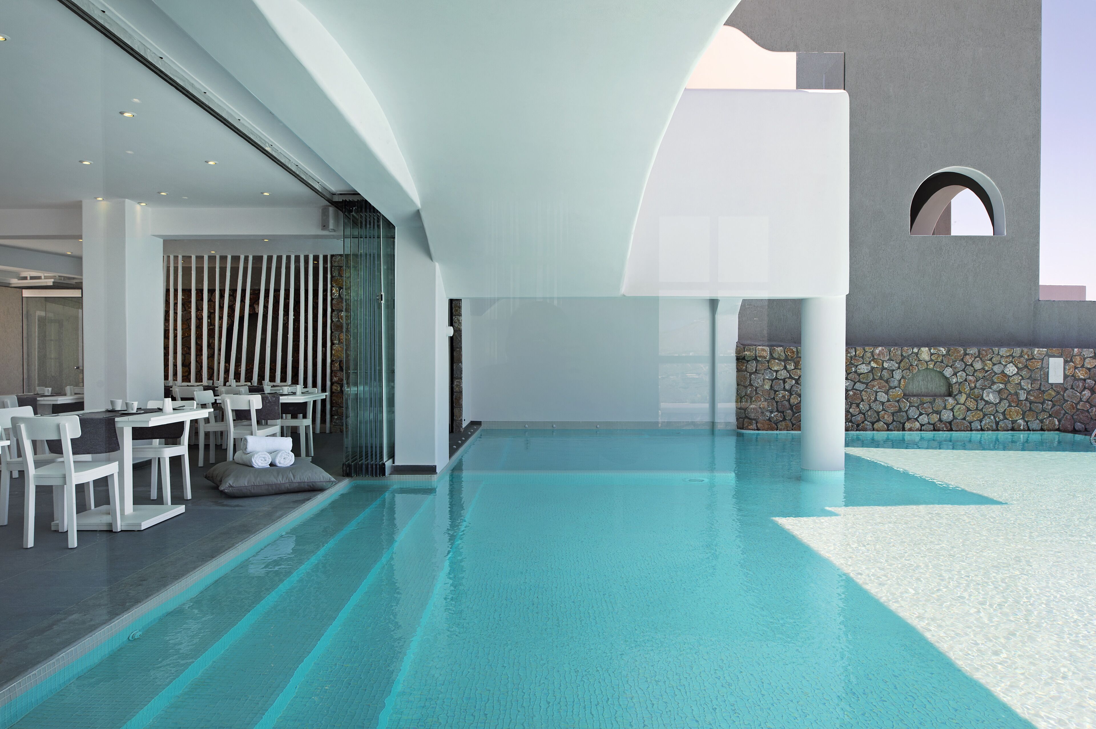 A modern indoor pool area with a dining setup and a stone wall.